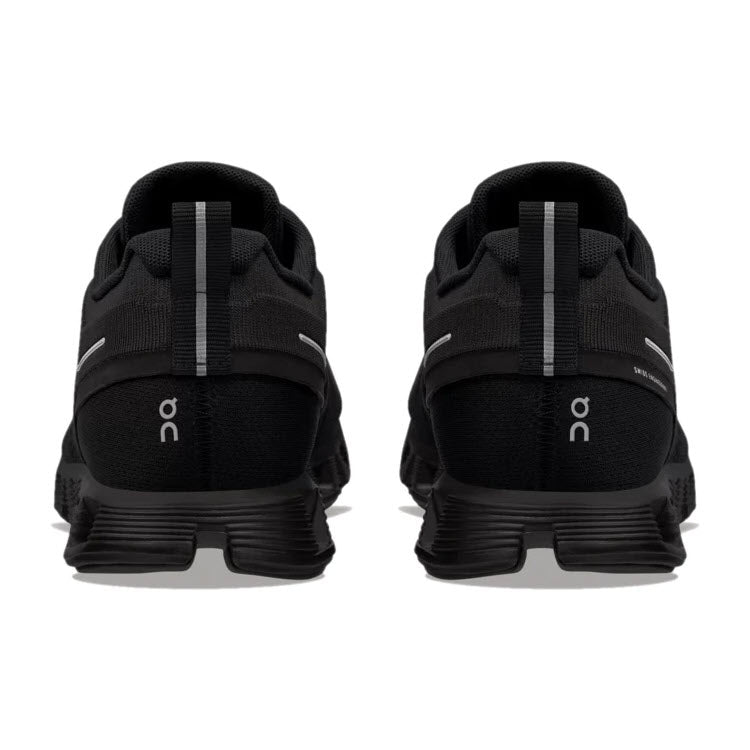 Rear view of a pair of ON CLOUD 5 WATERPROOF ALL BLACK running shoes by On Running, featuring white accents, CloudTec cushioning, and the letters &quot;ON&quot; on the heels.