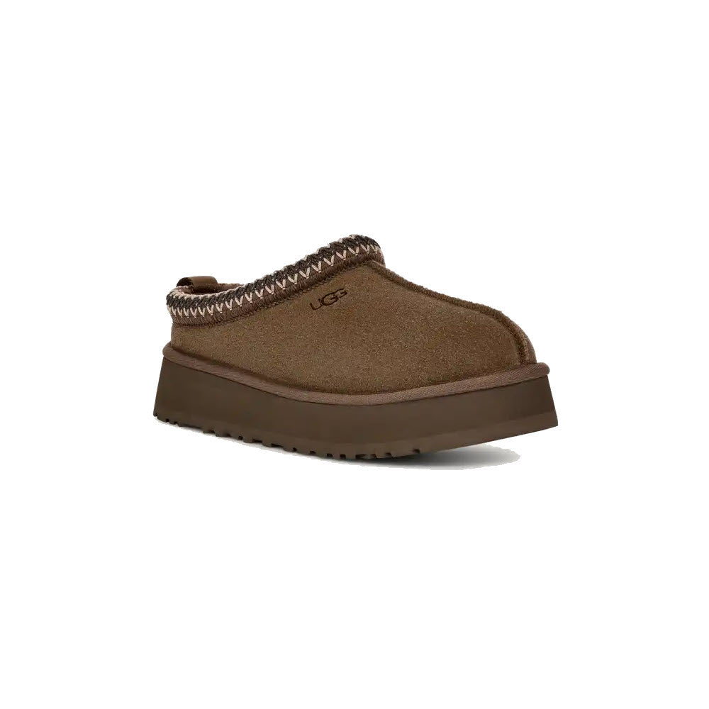 The UGG Tazz Hickory - Womens is a single brown clog with a thick platform outsole and woven detail around the ankle opening, featuring UGGplush™ lining for added comfort and labeled with the brand name &quot;UGG&quot; on the side.