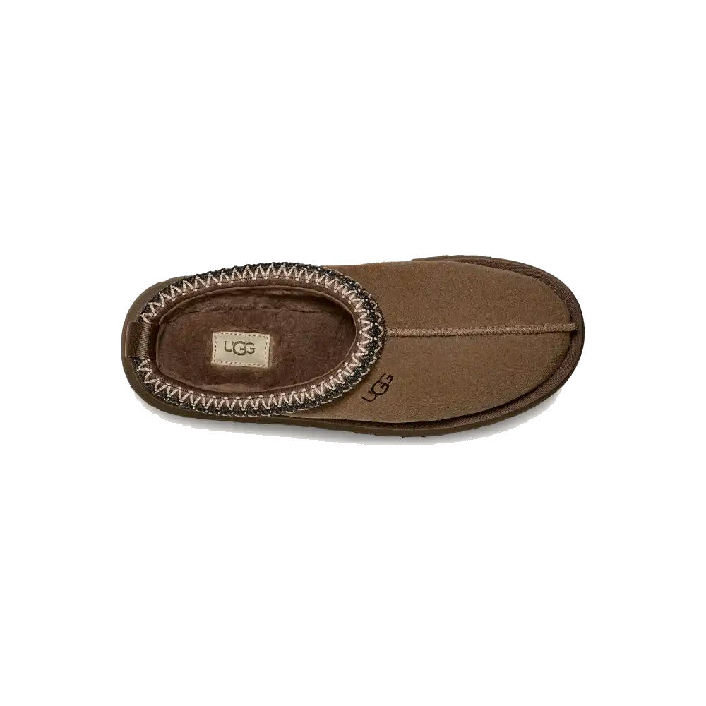 A single UGG TAZZ HICKORY slipper for women, featuring a fuzzy UGGplush™ lining and a stitched, rounded toe in brown. The UGG logo is visible on the inner sole and outer side of the slipper.