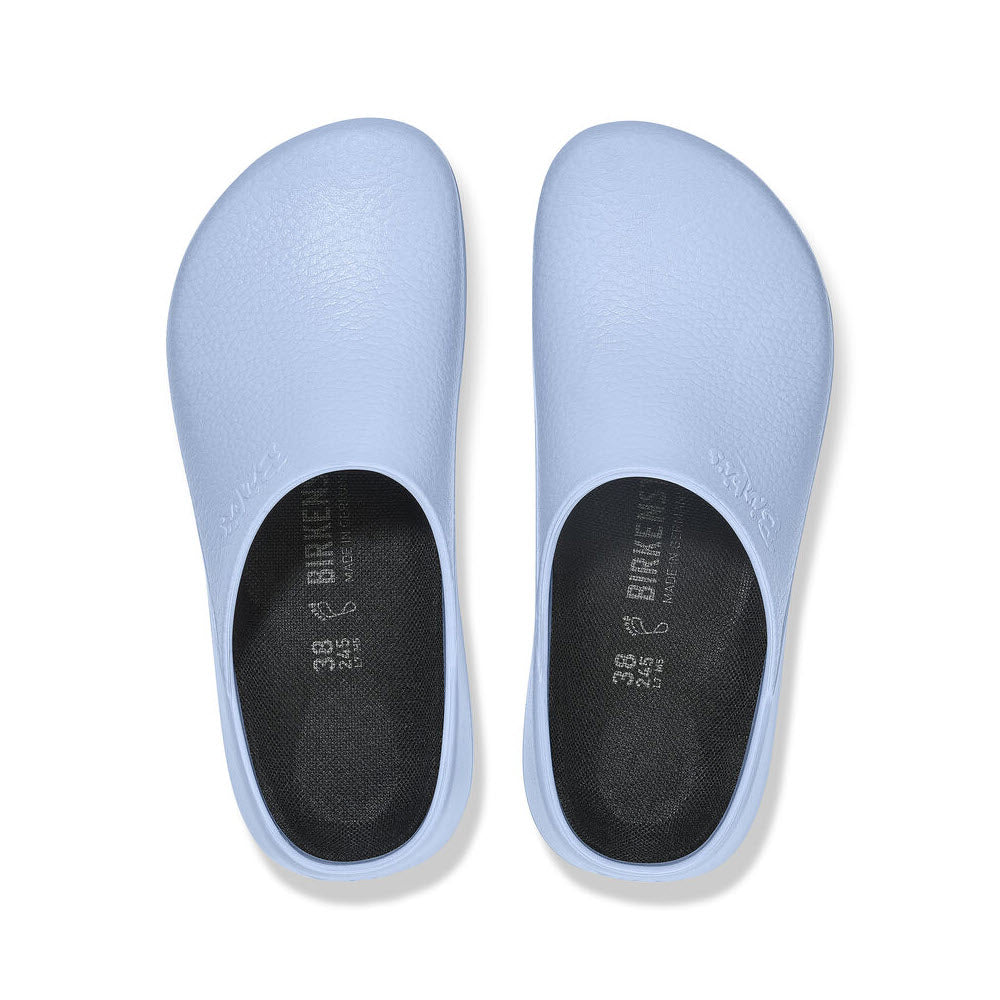 A pair of light blue BIRKENSTOCK SUPER BIRKI DUSTY BLUE - WOMENS with black insoles, viewed from above. The left clog has &quot;Birkenstock&quot; and size information embossed on the footbed, offering anatomic support and fluid-resistant PU for maximum comfort and durability.