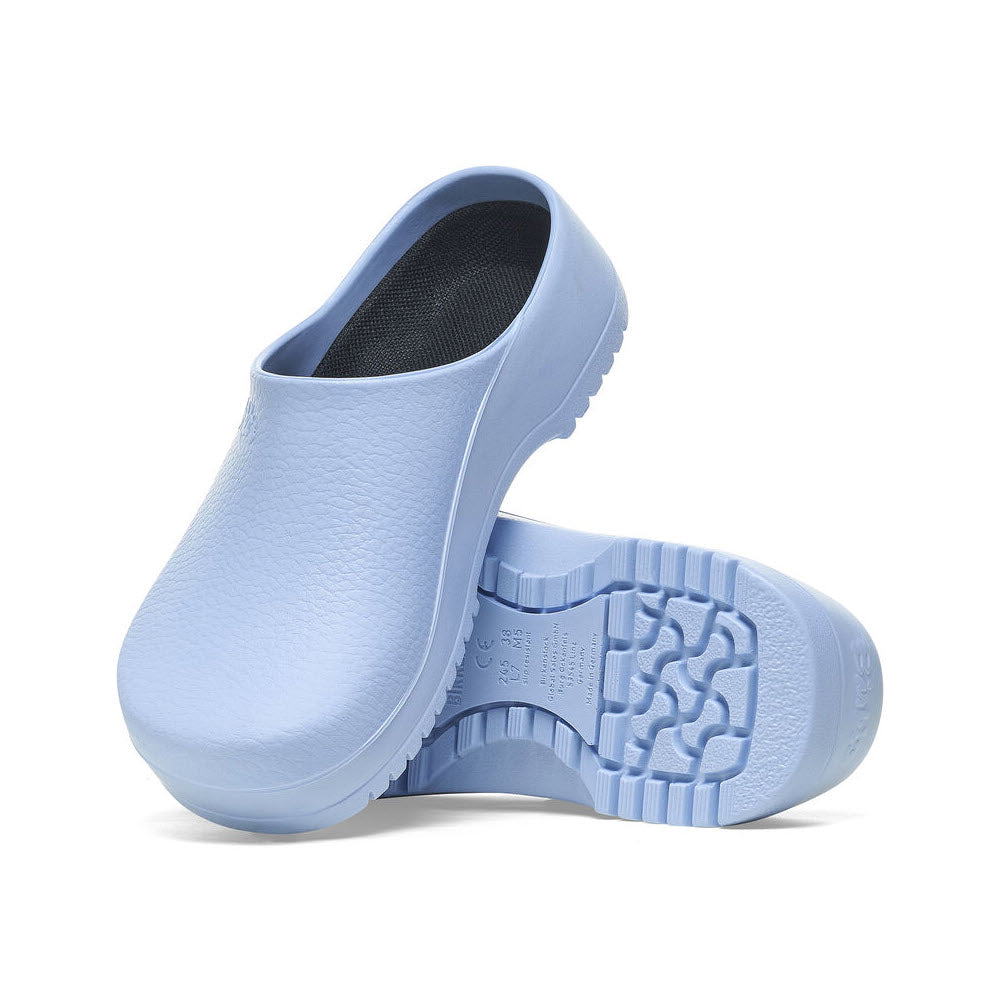 Two light blue Birkenstock Super Birki Dusty Blue - Womens clogs; one resting on its sole and the other placed on top, showcasing the textured outsole. Designed with anatomic support and crafted from fluid-resistant PU, these clogs combine comfort and durability perfectly.