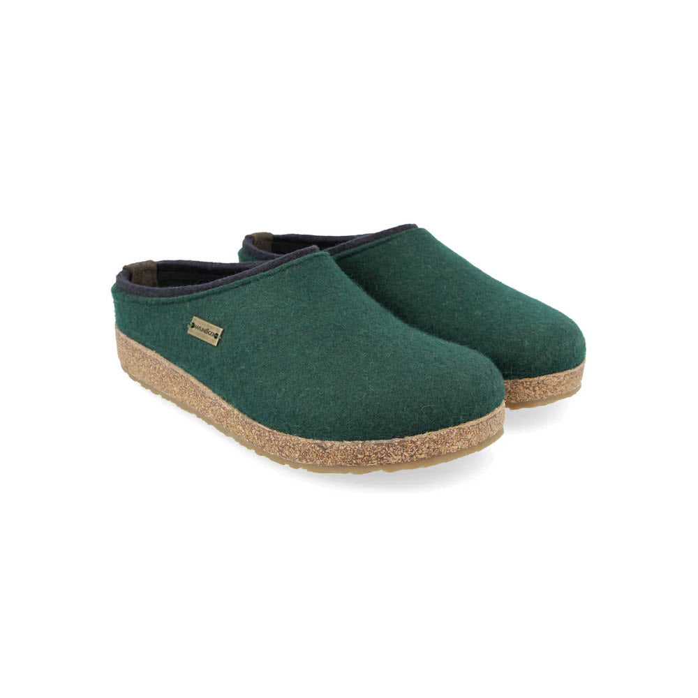 A pair of Haflingers Kris slip-on clogs in fir green with a blue trim, featuring a brown cork footbed and a small visible brand tag on one shoe.