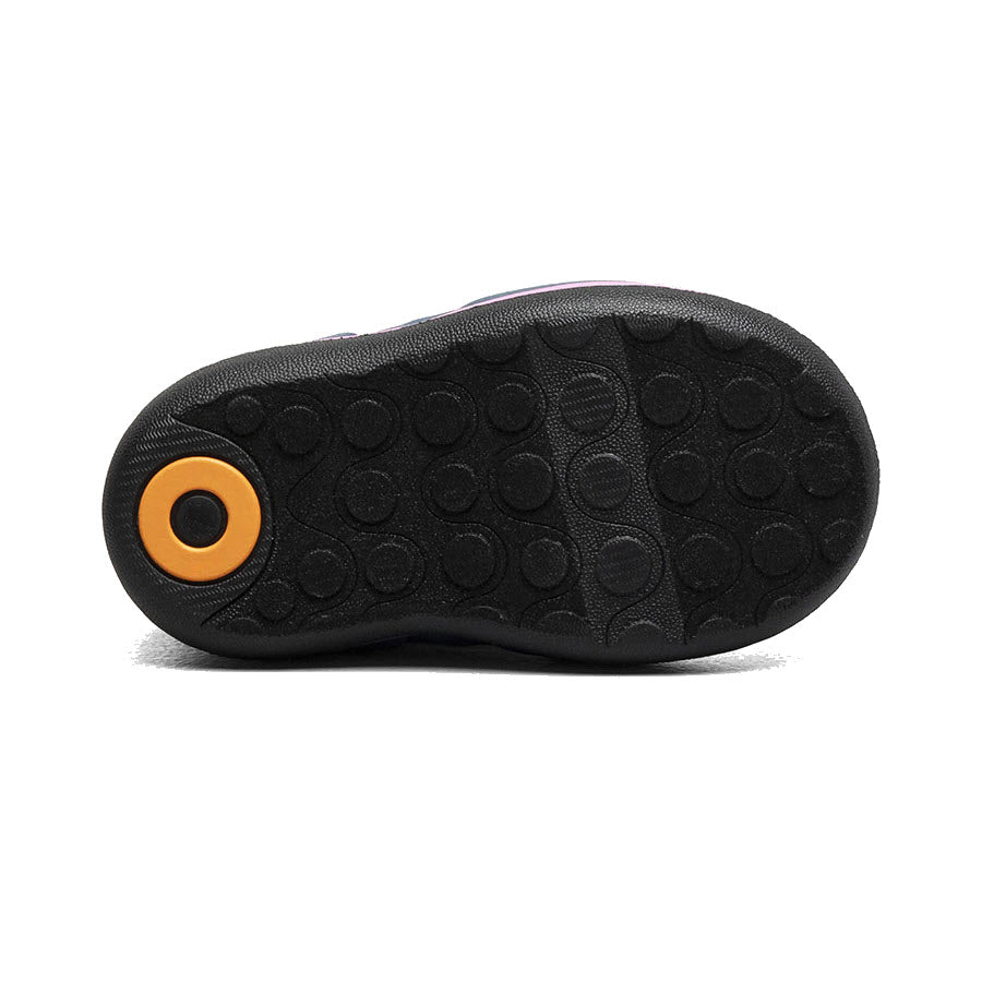 The image shows the sole of a BOGS BABY CLASSIC UNICORN MEADOW - KIDS black shoe with a circular yellow accent on the heel and a textured pattern of raised circles, designed to be ultra-lightweight and toddler-ready by Bogs.