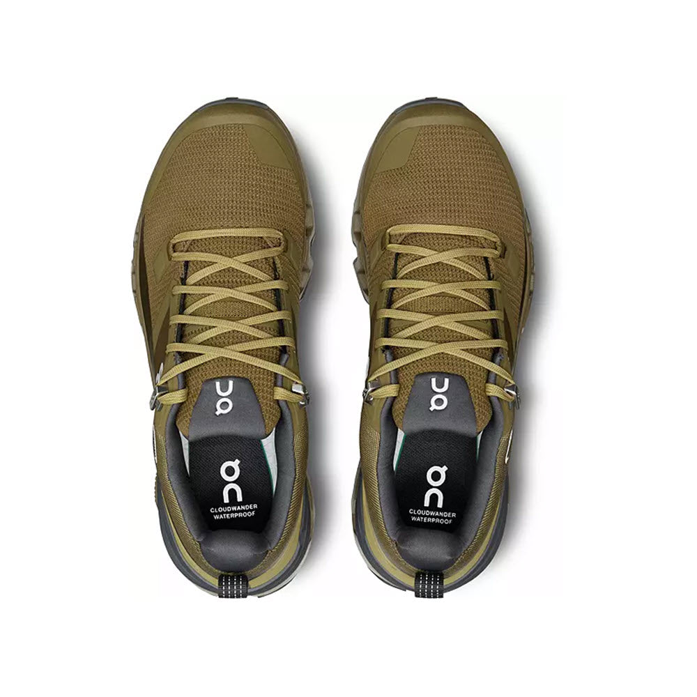 A pair of the ON CLOUDWANDER WATERPROOF HUNTER/SAFARI - WOMENS athletic shoes by On Running, viewed from above, showcasing the top laces and brand logo on the tongue, designed as a lightweight outdoor performance shoe.