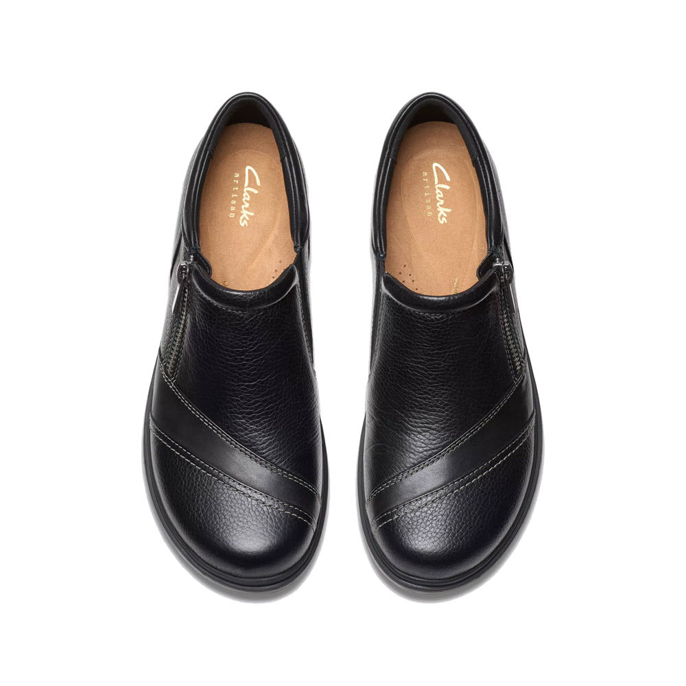 The Clarks Certina Pure Black women&#39;s shoes feature a sleek slip-on design with rounded toes and side zippers. Made from premium leather, they are adorned with the &quot;Clarks Collection&quot; label on the inner soles and are shown from an overhead view.