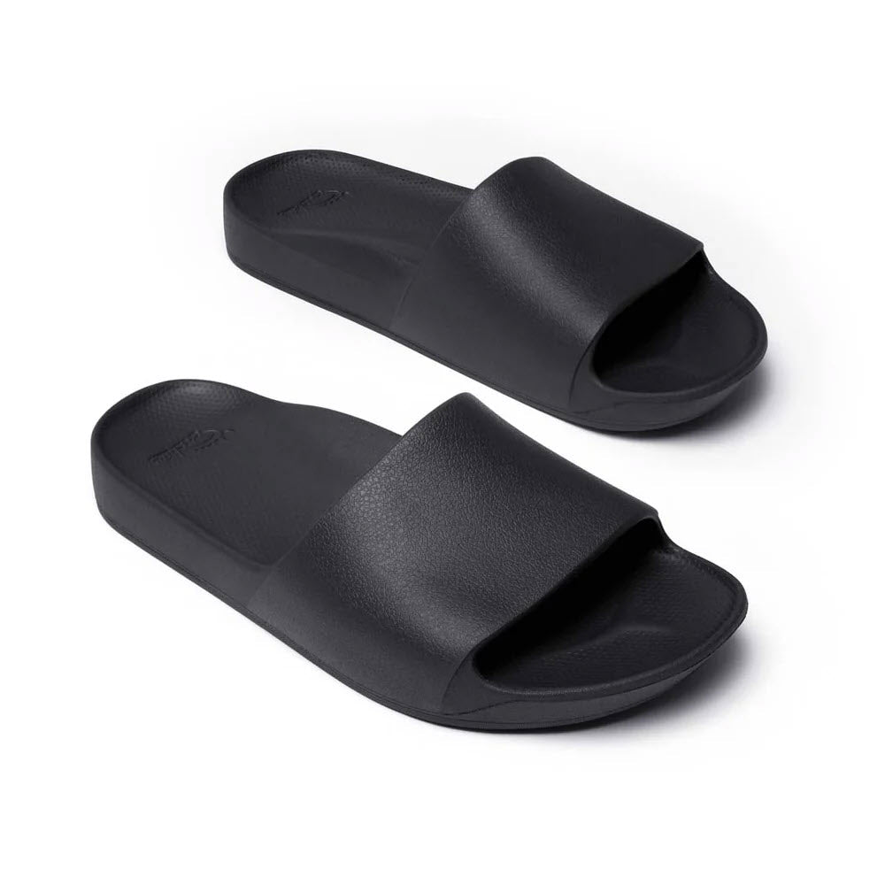 A pair of durable black Archies slide sandals with wide straps and textured footbeds, offering orthotic support for individuals with plantar fasciitis, are shown against a white background.