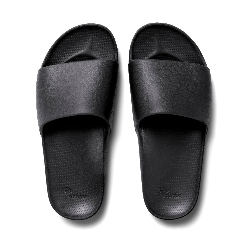 A pair of black ARCHIES SLIDES with a textured footbed and a wide strap across the top, offering durable orthotic support for those with plantar fasciitis, by Archies.