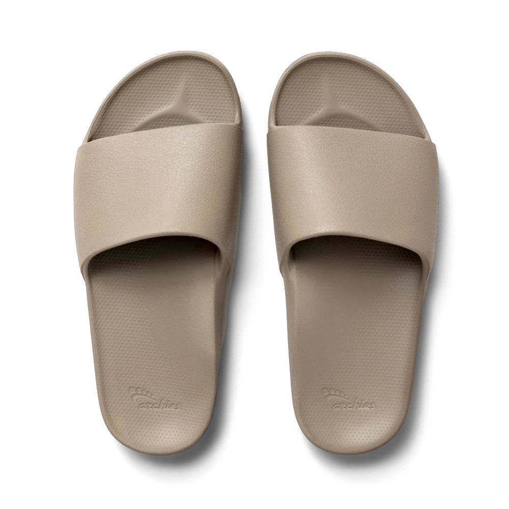 A pair of beige Archies ARCHIES SLIDES with orthotic support, featuring textured footbeds and wide straps for comfort and support.